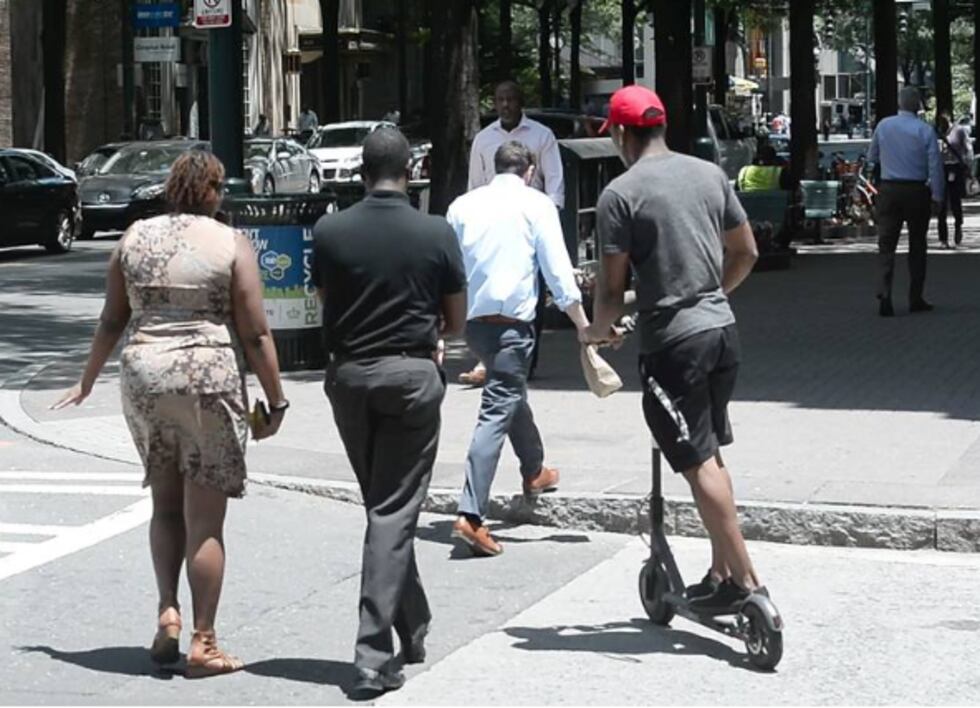 People riding scooters are zipping along Charlotte sidewalks and streets past pedestrians and...